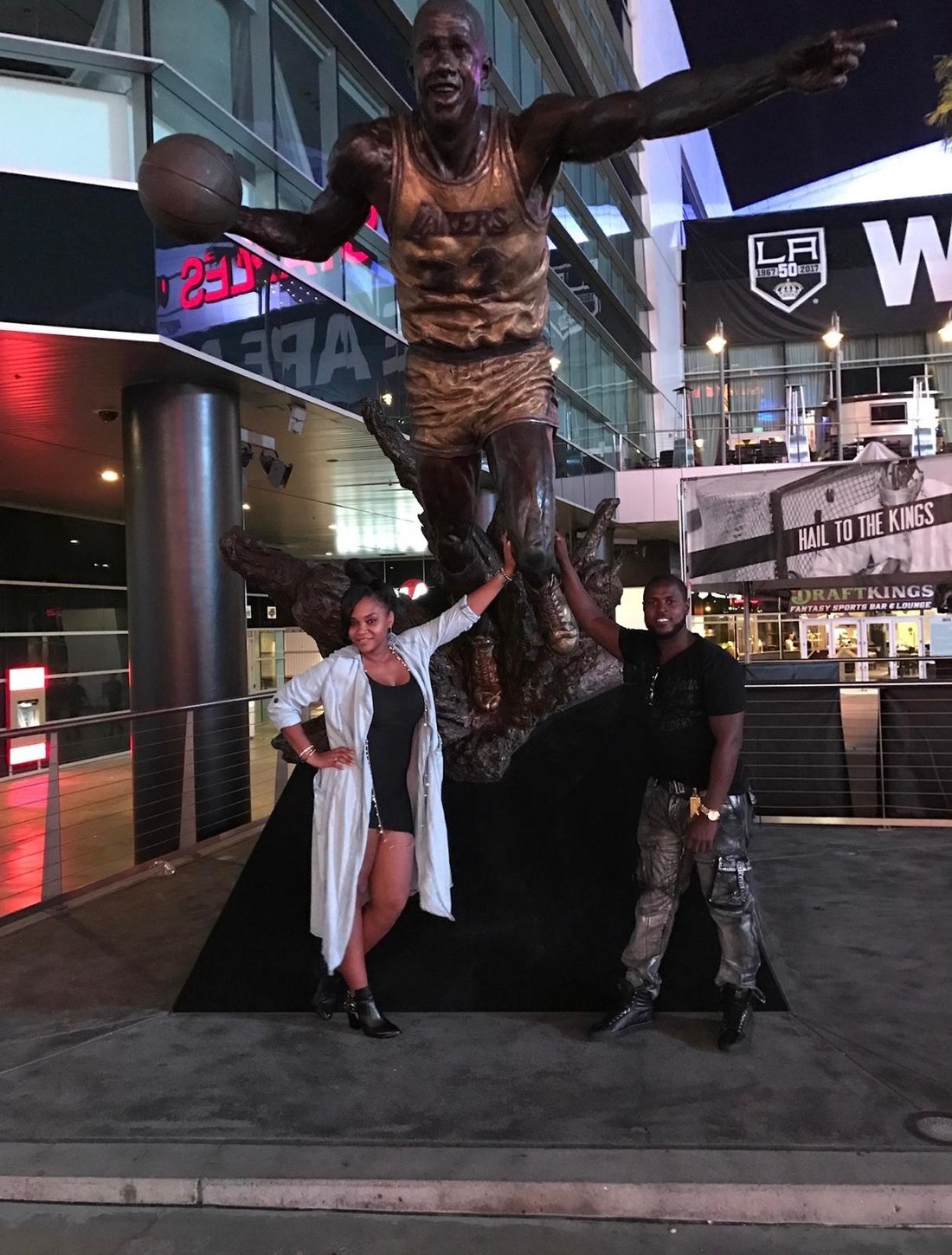 Eugene and Jessica posing at a bronze basketball statue at night